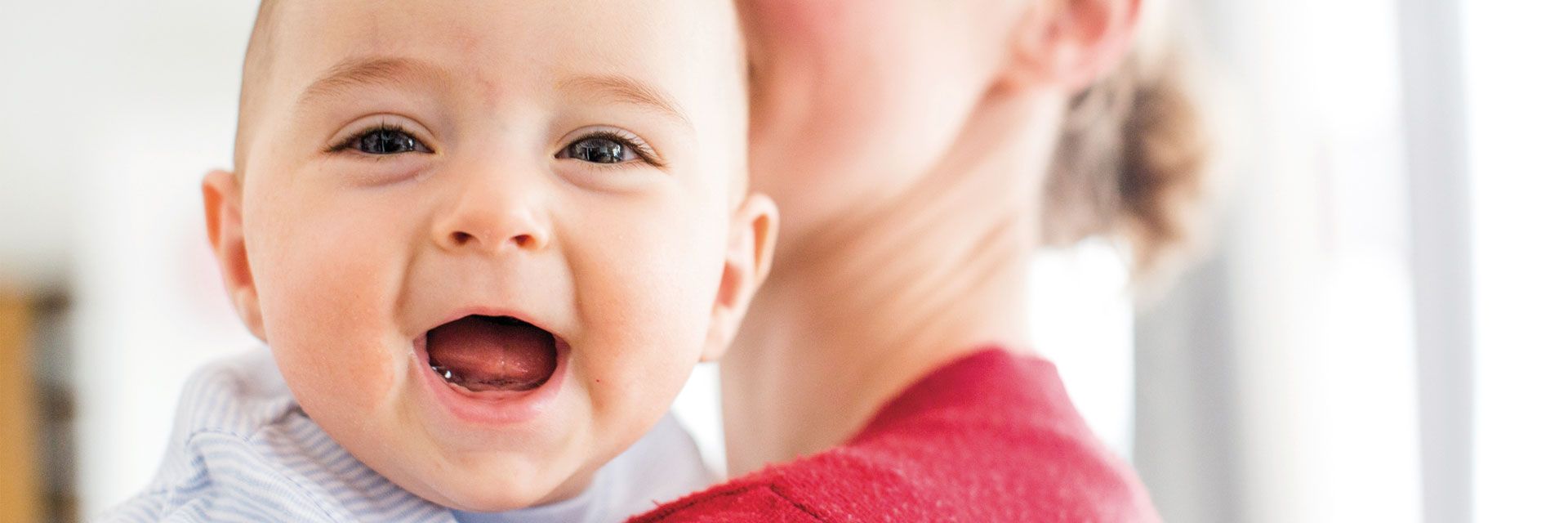 Foto: Ein Kleinstkind blickt mit strahlendem Lachen über die Schulter der Mutter.